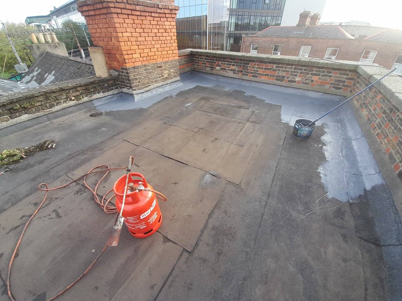 A felt covered flat roof in Dublin being sealed with a rubber coating. A gas canister is being used to heat the felt.