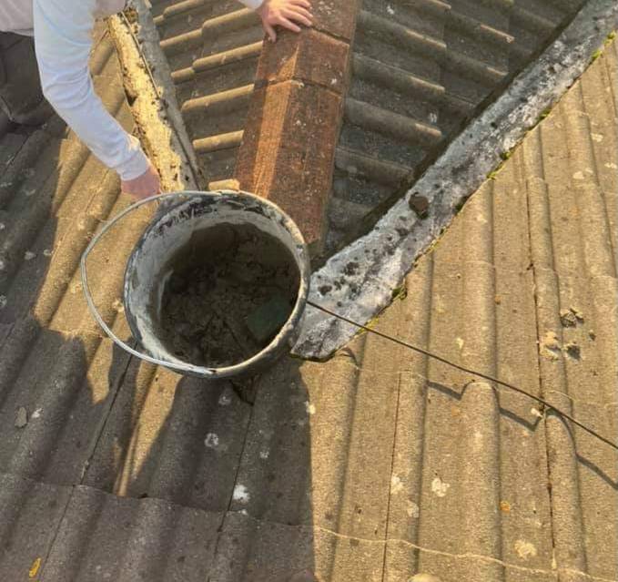 A bucket filled with mortar being used to repair a ridge tile on a roof